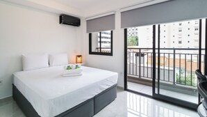 Une chambre moderne avec un grand lit, une table de chevet avec une lampe et une vue sur la ville grâce à de grandes fenêtres.