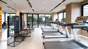 Une salle de sport équipée de tapis de course, de vélos d’exercice et d’un mur recouvert de miroirs.