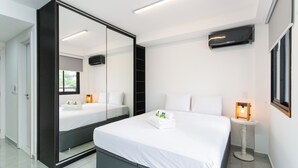 Une chambre d’hôtel moderne dotée d’un grand lit, d’un dressing, d’une table de chevet avec une lampe et d’un grand miroir.