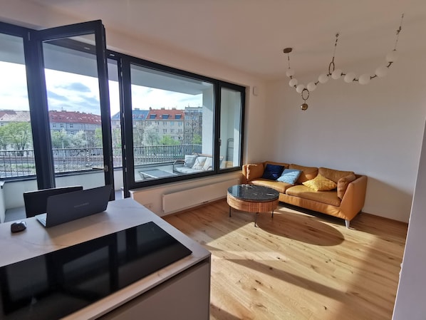 A modern living room with a large window, a sofa, a coffee table, and a laptop on a desk.