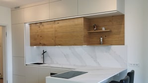A modern kitchen with a wooden upper cabinet, a marble backsplash, and a white island with bar stools. - Free Parking, Center Location, Nuslesky Pivovar Sunset Balcony Home (Prague)