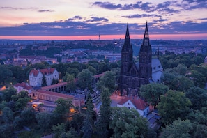 A historic cityscape with prominent Gothic architecture, including twin spires and a cathedral, surrounded by lush greenery and residential buildings.