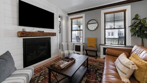 A living room with a fireplace, a television mounted on the wall, a striped chair, a sofa, and a coffee table.