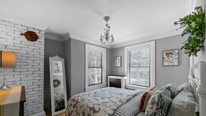 A bedroom with a brick wall, a chandelier, a bed with patterned bedding, and a radiator.