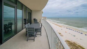 Un balcon avec une table et des chaises, donnant sur une plage parsemée de parasols et sur une jetée.