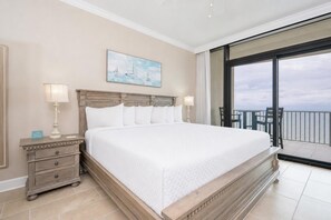 A large bed with a wooden headboard, two bedside tables with lamps, a painting on the wall, and a balcony with a view.