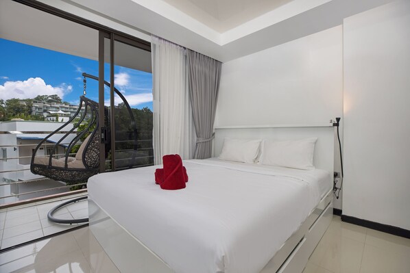 A hotel room with a bed, a red towel, a balcony with a hanging chair, and a view of buildings. - Chill & Relax Stay at Rawai Condo 311 (Rawai)