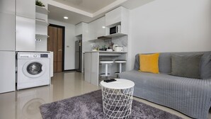 A modern kitchen with a washing machine, a grey sofa with yellow cushions, and a small white table. - Chill & Relax Stay at Rawai Condo 311 (Rawai)