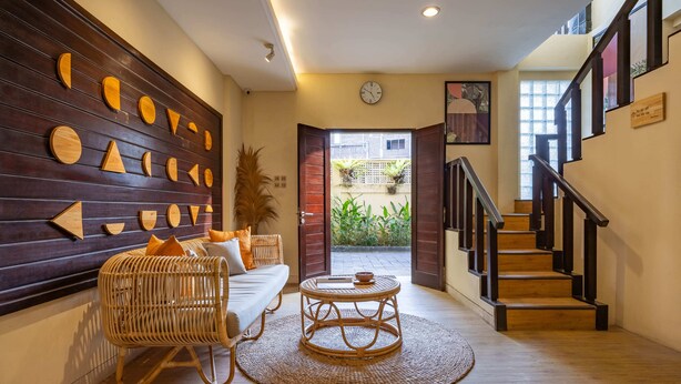 A modern interior with a wooden wall, a wicker sofa, a round table, and a staircase. - Cove Kavana (Tibubeneng)