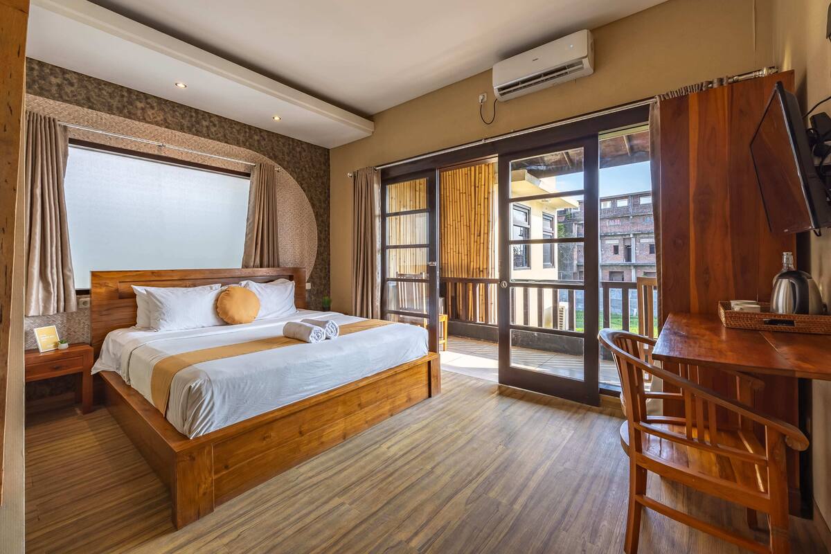 Quarto de hotel com cama de madeira, uma escrivaninha e vista para o exterior.