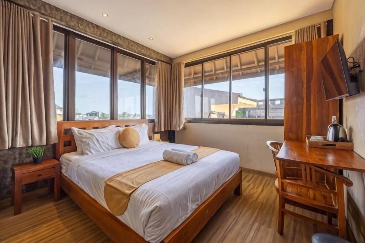 Quarto de hotel com cama grande, escrivaninha de madeira e vista para a cidade.