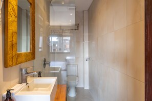 A modern bathroom with a large mirror, a sink, a toilet, and a shower. - Cove Kavana (Tibubeneng)