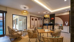 A modern interior with wicker furniture, a wooden dining table, and a kitchen area with a white cabinet and decorative items. - Cove Kavana (Tibubeneng)