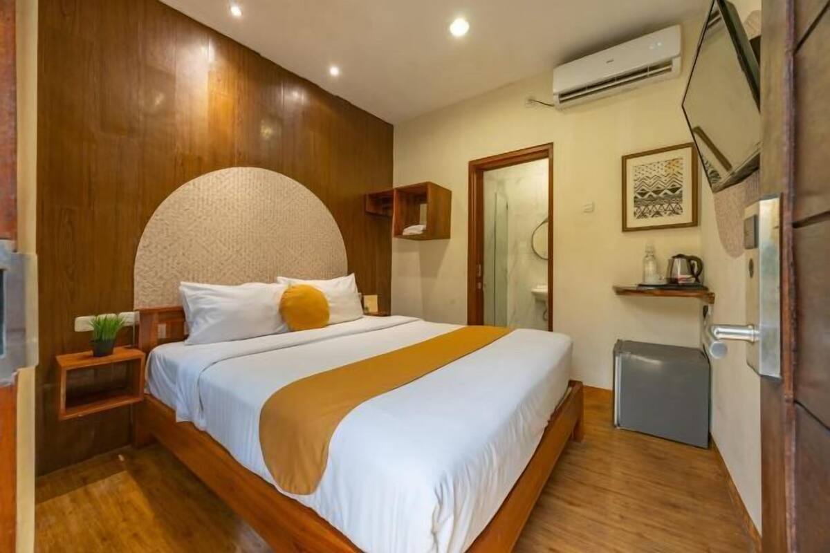 Quarto com cama, mesa de cabeceira e uma pequena geladeira.