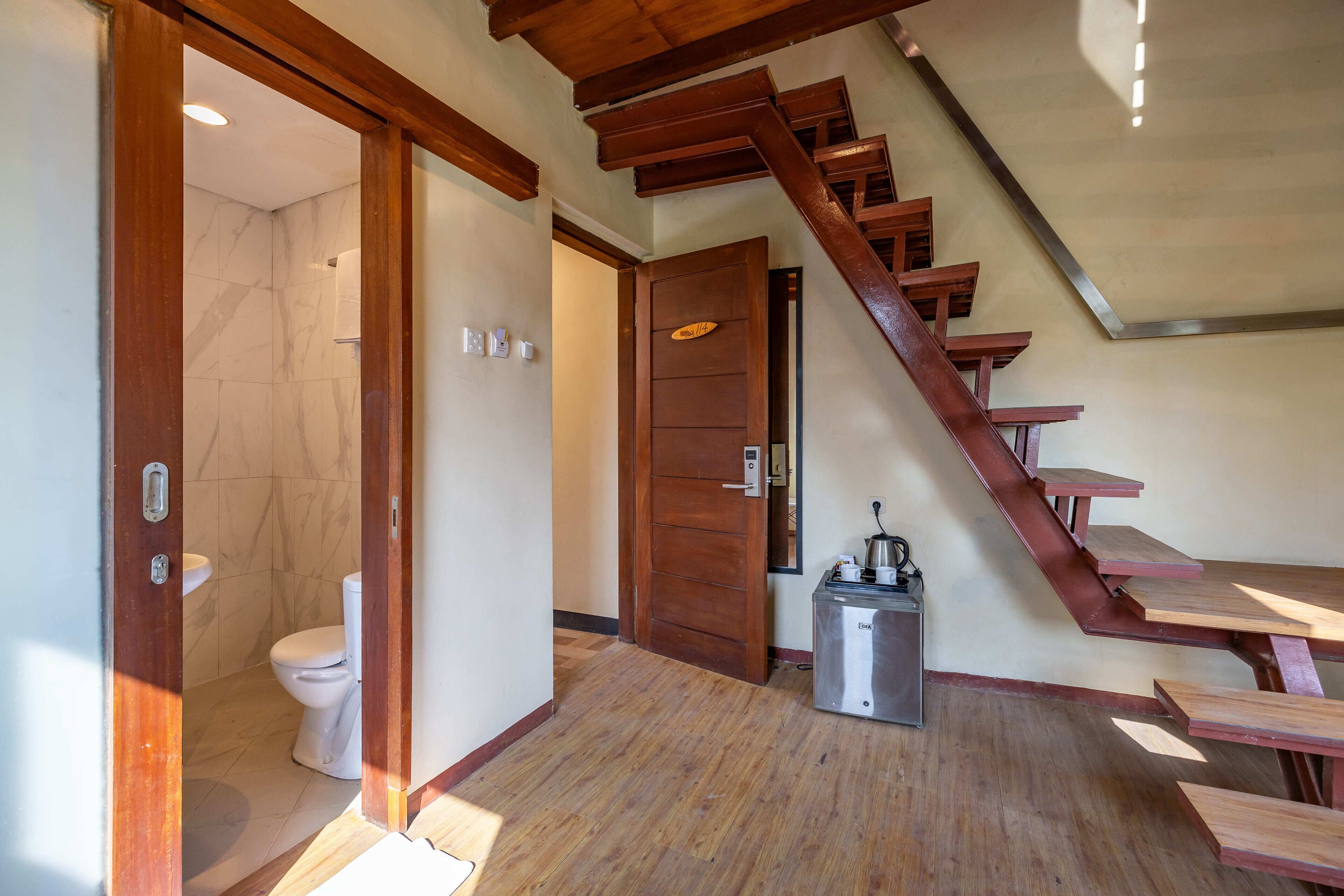 A wooden staircase leading to a second floor, a small kitchenette with a refrigerator, and a bathroom with a toilet and shower.