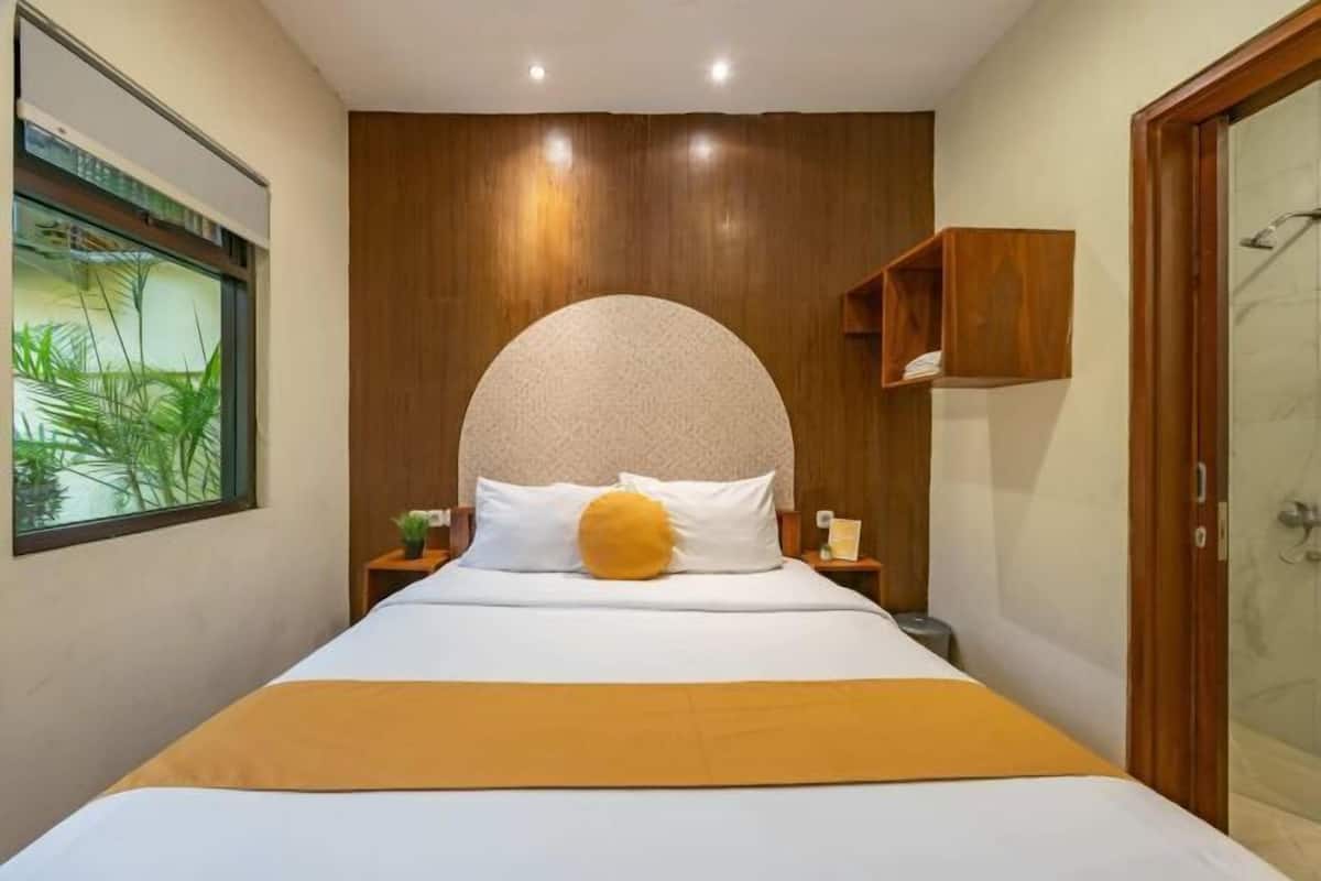Quarto moderno com uma cama grande, cabeceira de madeira, mesa de cabeceira pequena e janela com vista para áreas verdes.