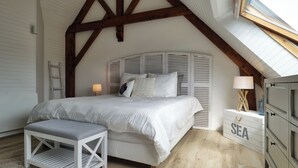A bedroom with a sloped ceiling, a bed with a headboard, a bench, a dresser, and a skylight.