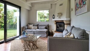 A spacious living room with a glass door leading to a garden, a fireplace, and a comfortable seating area.