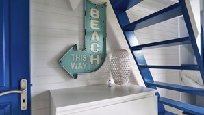 A room with a white dresser, a teal sign reading "BEACH THIS WAY", and a blue ladder.
