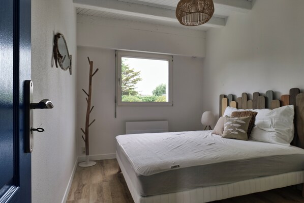 Un dormitorio con cama, ventana, puerta y una lámpara fijada a la pared.