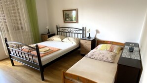 Quarto com duas camas, mesa de cabeceira, cômoda, um quadro na parede e janela com cortinas leves.