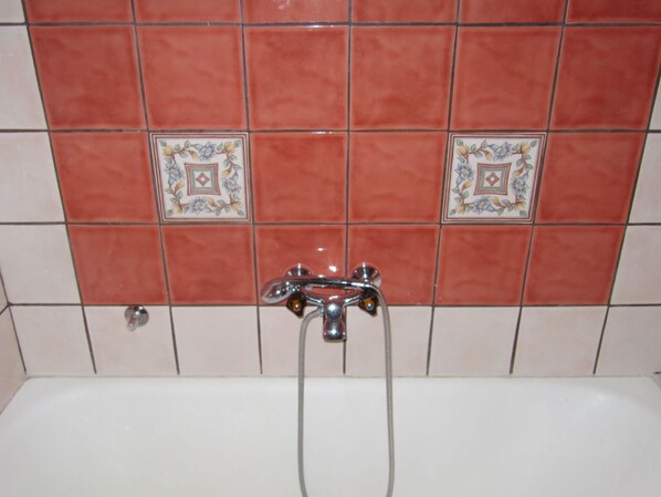 A bathroom with a white bathtub, a shower, and a tiled wall with floral patterns. - Apartment Marija 7 (Crikvenica)
