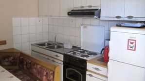 Cozinha compacta com armários brancos, fogão a gás, pia e geladeira.