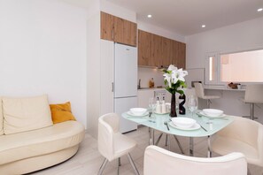 Een moderne keuken met houten kastjes, een witte koelkast, en een eethoek met een glazen tafel voor vier personen.