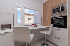 Een moderne keuken met witte kastjes, een houten accentmuur, een ingebouwde magnetron en een raam met uitzicht.