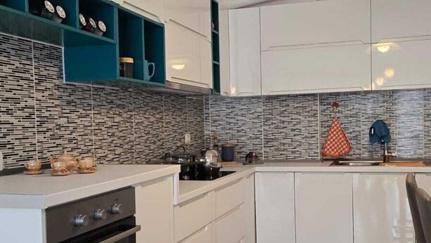 Une cuisine moderne avec des armoires blanches, un four encastré, une cuisinière et un pare-feu orné d’un motif en mosaïque.