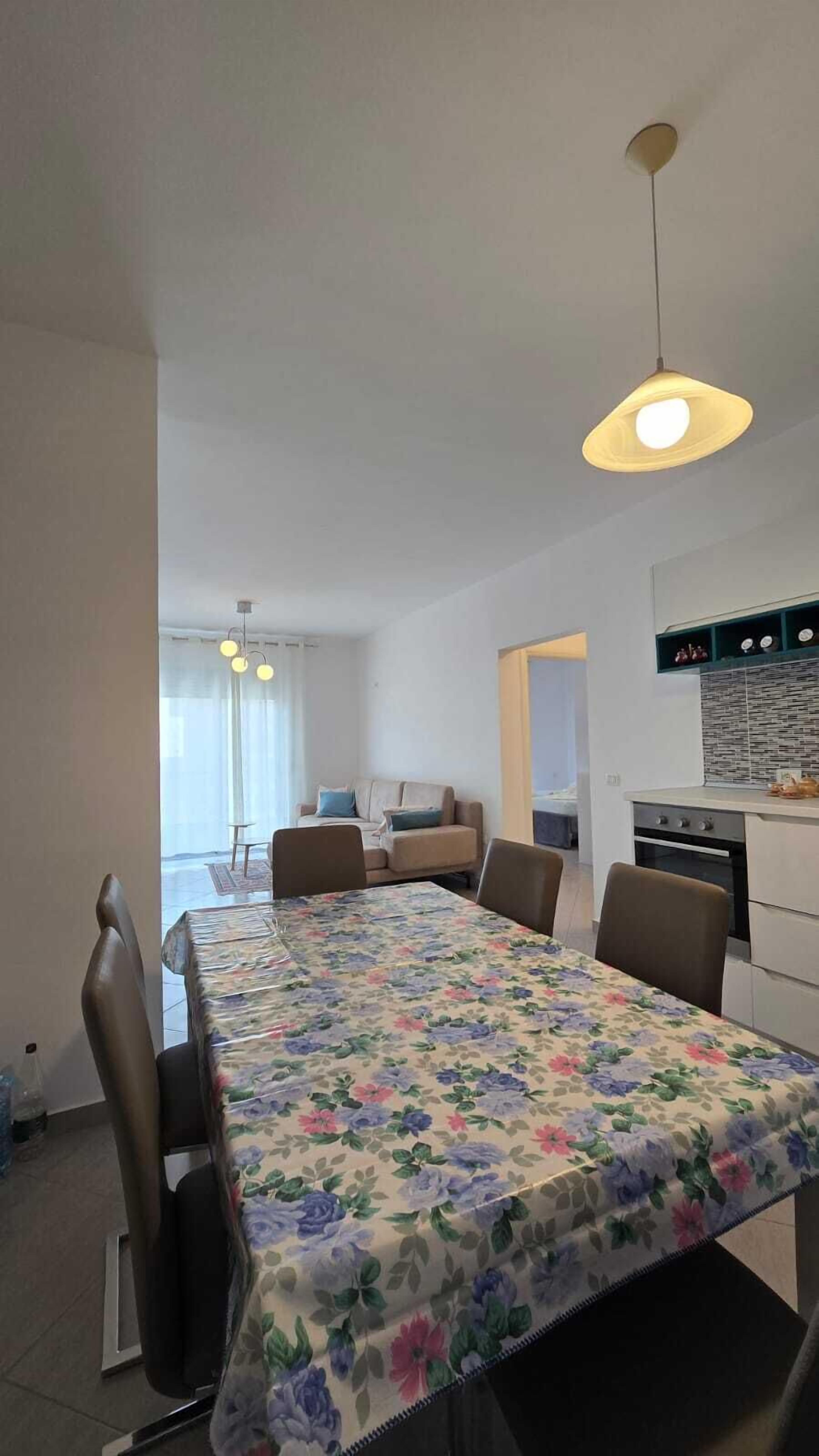 A dining area with a floral tablecloth, a sofa, and a kitchen in the background.
