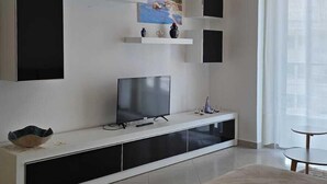 Un salon moderne doté d’un téléviseur à écran plat, d’un meuble de rangement blanc et d’un canapé beige.