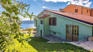 A house with a green exterior and a red roof, situated next to a body of water. - Studio Mistral 6 (Crikvenica)