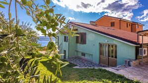 A two-story building with a tiled roof, a small garden area, and a view of the sea. - Studio Mistral 6 (Crikvenica)