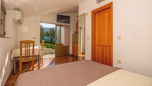 A room with a bed, a table with chairs, a wooden door, and a view of the outdoors. - Studio Mistral 6 (Crikvenica)