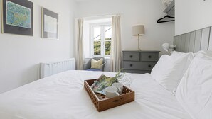Een keurig opgeruimde slaapkamer met een bed, een dressoir, een stoel en een raam met gordijnen.