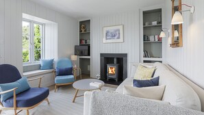 Een knusse woonkamer met een open haard, een bank, een fauteuil en een boekenplank.