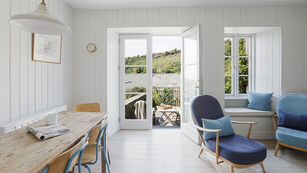 Een kamer met een houten eettafel, blauwe stoelen, een blauwe bank en uitzicht op een tuin door een glazen deur.