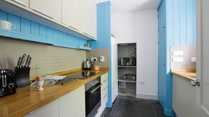 Compact kitchen with functional layout, featuring a toaster, kettle, and oven, along with ample storage in cabinets and a pantry.