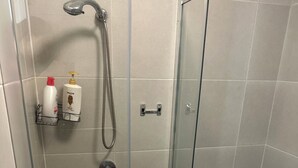 A modern bathroom with a glass-enclosed shower, a toilet, and a towel rack with toiletries. - Cozy and private one bedroom studio with double bed for couples or single (Busby)