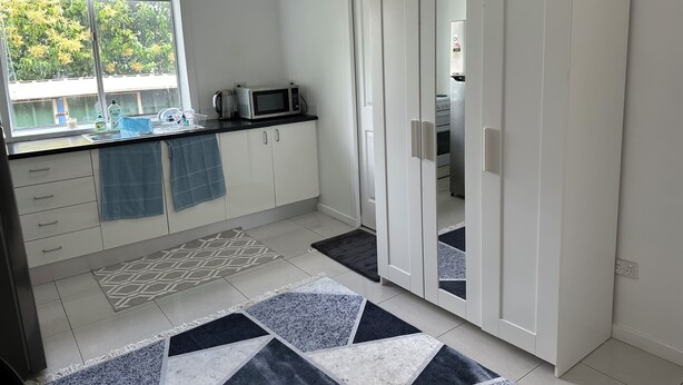 A compact kitchen with white cabinets, a microwave, and a stove. There is a window with a view of greenery outside. - Cozy and private one bedroom studio with double bed for couples or single (Busby)