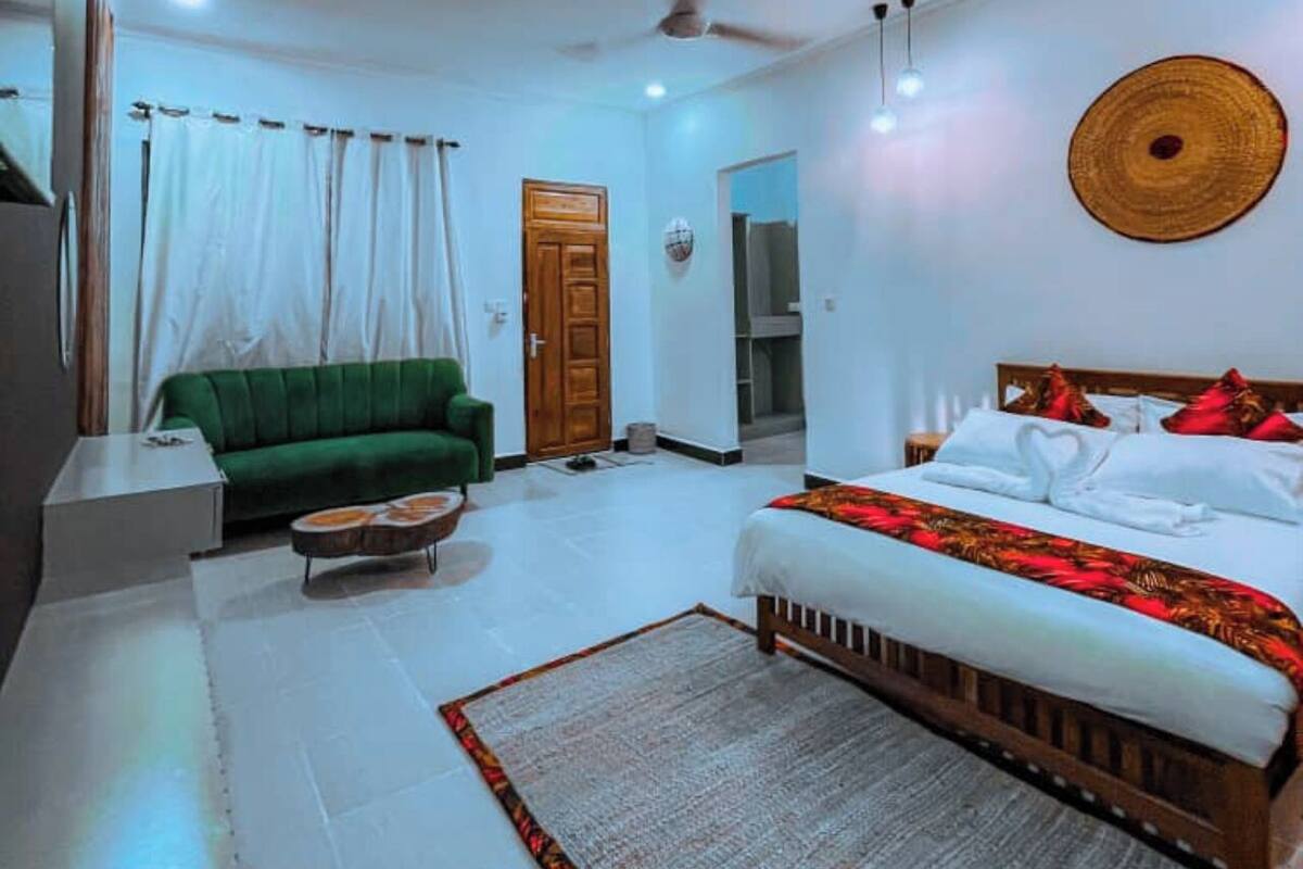 A bedroom with a bed, a green sofa, a wooden headboard, a ceiling fan, and a woven wall hanging.