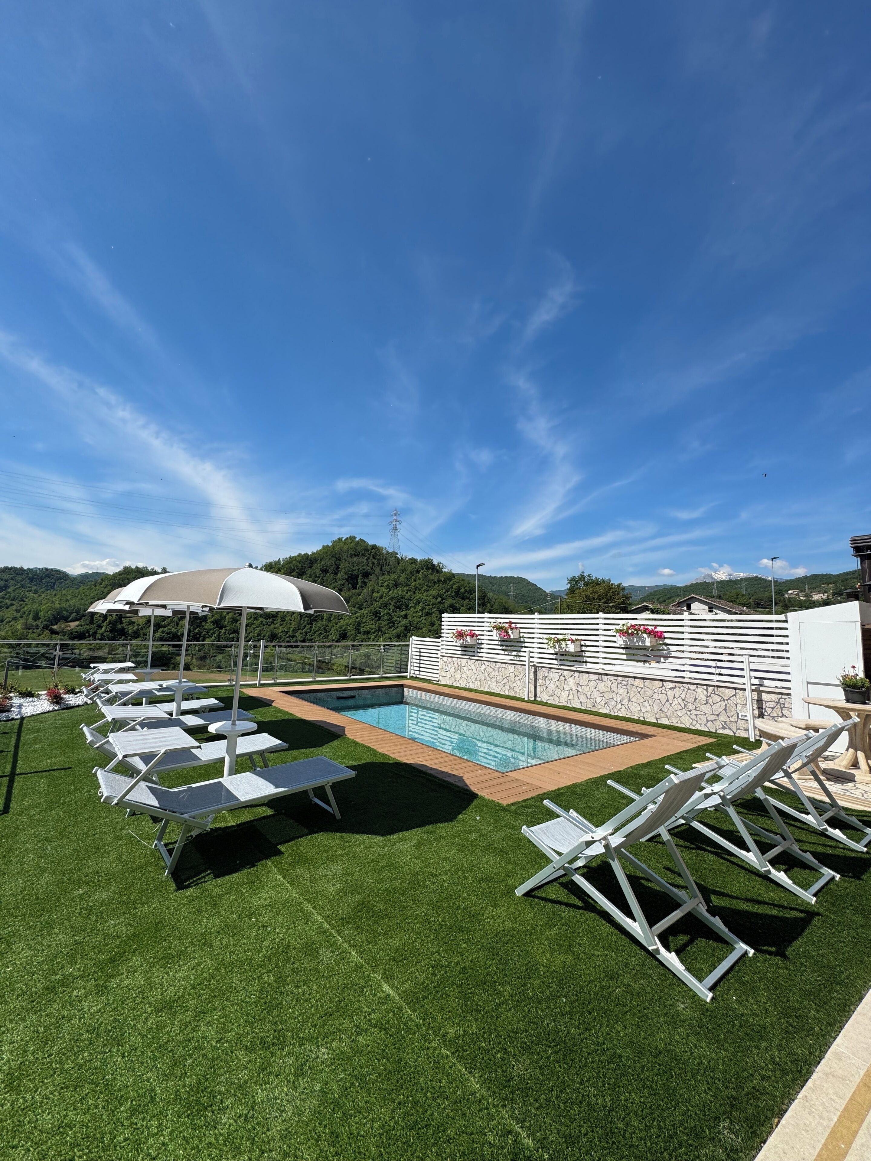 A pool area with artificial grass, lounge chairs, and umbrellas.
