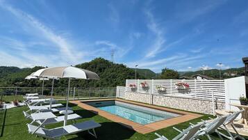 A pool area with artificial grass, lounge chairs, and umbrellas.