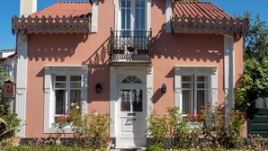 Ein rosafarbenes Gebäude mit einem Balkon, weißen Fenstern und einer Tür.