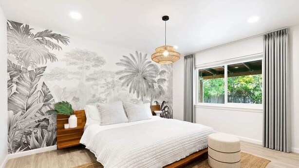 Une chambre moderne avec un grand lit, une fresque murale, un luminaire suspendu et une fenêtre avec des rideaux.