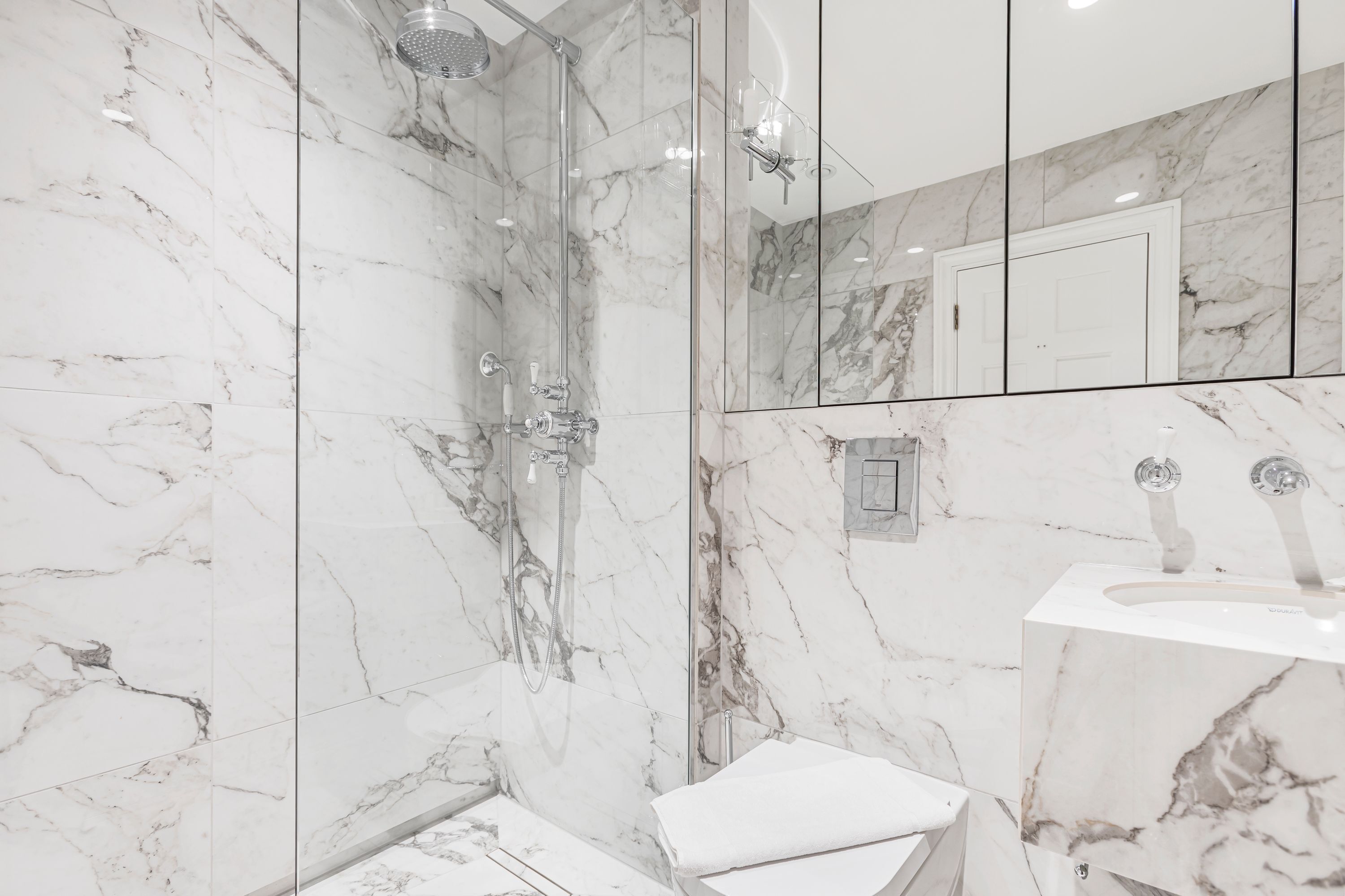 A bathroom with a glass-enclosed shower, a white toilet, and a marble sink.