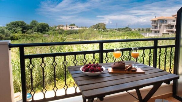 A balcony with a table set for breakfast, including a bowl of fruit and a glass of orange juice.
