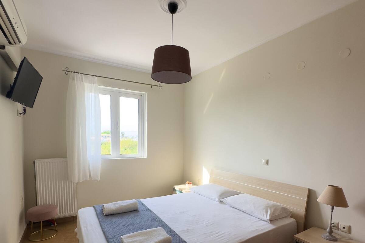 Habitación de hotel con cama, mesita de noche, lámpara y televisor fijado a la pared.