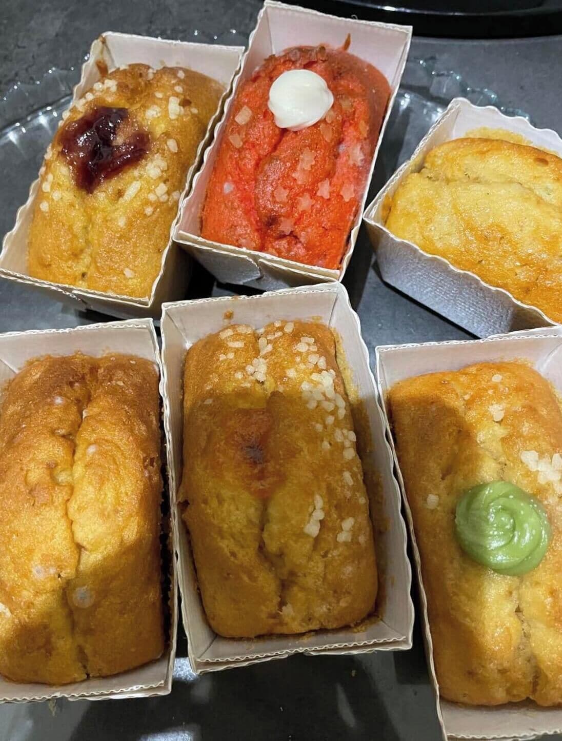 Six baked goods in paper containers.
